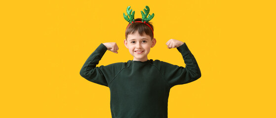 Funny little boy with reindeer horns on yellow background