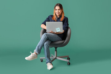 Transgender programmer with laptop sitting on chair against green background
