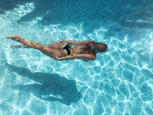 High Angle View Of A Woman Wearing A Bikini Swimming Underwater In An Outdoor Swimming Pool On A Hot Sunny Day