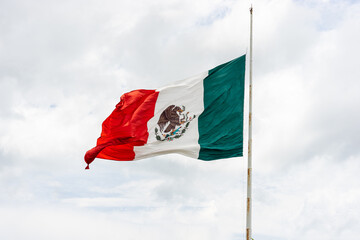 Wall Mural - Mexican flag waving on the flagpole with white cloudy sky, space for copy.