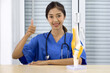 Young asian doctor in blue uniform and stethoscope raise finger thumb up with a smile. An anterior cruciate ligament on deluxe functional knee joint model is on the table.