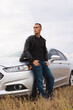 Handsome stylish man standing near his car at the field