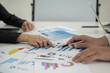 © maeching - Business people gather for a brainstorming meeting pointing to a graph to think about market data analysis.