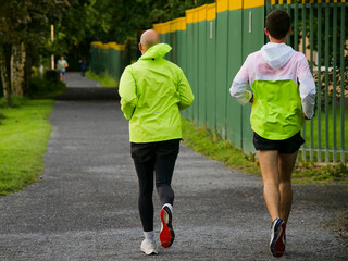 Two male runners in high visibility jackets running in a park. Sport activity. People jogging. Healthy lifestyle concept.