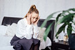 © irissca - Migraine Headaches At Work, Frequent Headache and Work Ability. Exhausted, Tired Businesswoman with headache after work sitting on bed at home. Business woman at office feeling sick at work