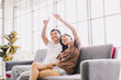© Pun - Cute couple in love thinking about something on sofa at home. Handsome man hugging his girlfriend and planning the future on a couch in beautiful living room. Asian couple future plan.