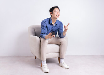 Poster - Young Asian man sitting on armchair on white background