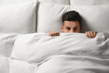 Sticker - Handsome man covering his face with blanket while lying in bed at home