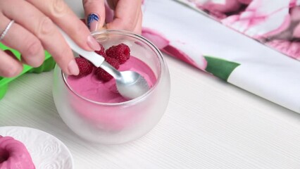 Wall Mural - A woman scoops dessert from a mug with a spoon. Soufflé with cottage cheese and raspberries. Decorated with berries. The camera moves on a slider. Close-up.