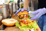 Fototapeta Kwiaty - Making burgers. Preparing a hamburger in a protective gloves, in a food truck, in a fast food restaurant, close up.