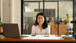 © Prathankarnpap - Cheerful asian female employee sitting with arms crossed at her office desk and smiling at camera