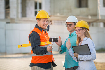 men and a woman in yellow and white helmets, blue shirts are standing at a construction site with do