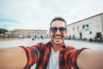 Wall Mural - Handsome young man taking selfie on city street - Happy smiling guy portrait walking outdoors