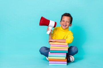 Poster - Full length photo of small cheerful boy sitting floor pile stack book hand hold loudspeaker isolated on cyan color background