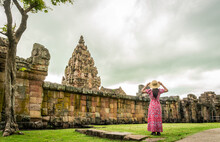 Young Tourist Wearing A Red Floral Dress Stands Holding A Hat In Front Of Phanom Rung Prasat Hin Phanom Rung. Buriram Province Thailand