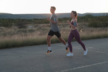 healthy young couple jogging in the city streets in the early morning with a beautiful sunrise in the background. 