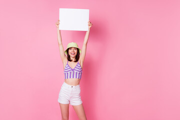 Poster - Photo portrait of lovely young girl holding white paper sheet empty space dressed trendy singlet cap isolated on pink color background