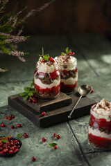 Latvian, scandinavian traditional rye whole grain bread layered dessert with whipped cream and cowberry jam served in glass jars on brown wooden board, table with berries, copy space.