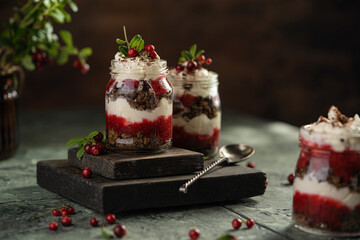 Latvian, scandinavian traditional rye whole grain bread layered dessert with whipped cream and cowberry jam served in glass jars on brown wooden board, table with berries, copy space.