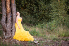Beautiful And Sensual Young Caucasian Woman Wearing A Yellow Evening Dress Outside In A Natural Setting Over A Heather And Forest Background. High Quality Photo