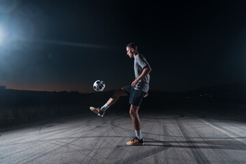 portrait of a young handsome soccer player man on a street playing with a football ball.