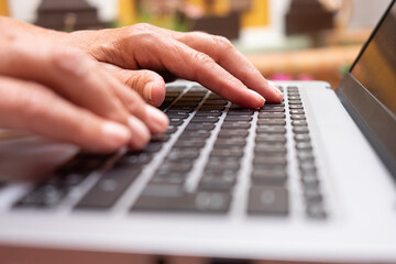 Mature woman's hands typing on laptop keyboard browsing the net