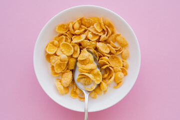 Canvas Print - top view of bowl with corn flakes, milk and spoon on pink background.