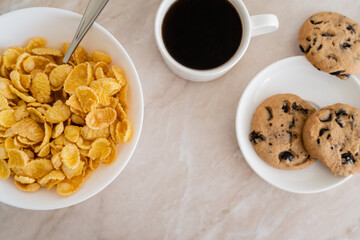 Wall Mural - top view of bowl with corn flakes near chocolate chip cookies and cup of coffee on marble surface.