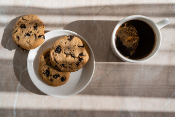 Wall Mural - top view of cup of black coffee near white saucer with chocolate chip cookies on marble surface.