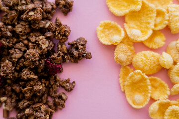 Wall Mural - top view of crispy corn flakes and crunchy granola isolated on pink.