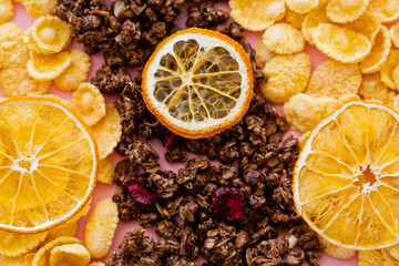 Wall Mural - top view of crispy corn flakes and tasty granola near dried oranges on pink.