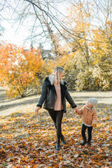 Wall Mural - Happy mother and daughter are walking in the autumn park. Beautiful family in warm clothes. Fall.