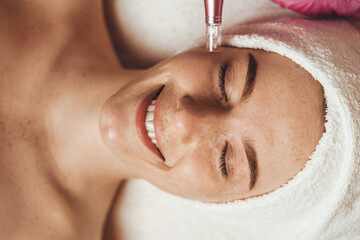 freckled woman face receiving mesotherapy injection with derma pen on face for rejuvenation on the s