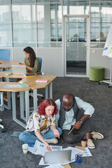 Poster - Young businesswoman pointing at laptop screen during presentation of new project points and discussing them with African American man