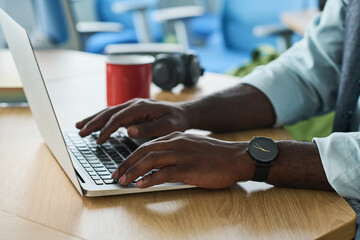 Aufkleber - Hands of young African American businessman typing on laptop keypad while sitting by workplace in office and searching for online data