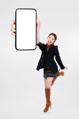 Asian woman dressed in Korean style on white background, a smiling face doing jumping gesture expressing joy or persuasion, showing a blank mobile screen with blank space for mobile apps on screen.