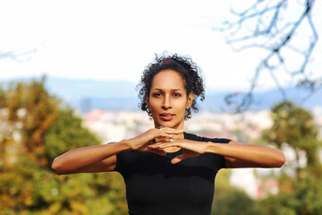 close up woman outdoors with earphones and curly hair hands on chest sports outfit