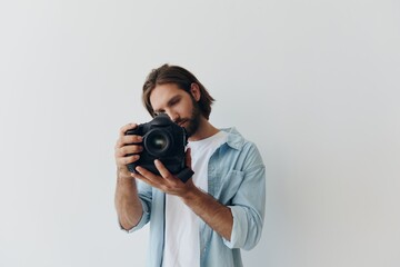 Poster - Man hipster photographer in a studio against a white background holding a professional camera and setting it up before shooting. Lifestyle work as a freelance photographer