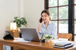 © Katcha - Female freelance is talking with colleague on smartphone and typing information on laptop while working