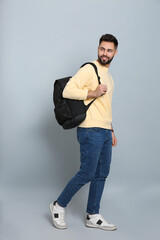 Wall Mural - Young man with stylish backpack walking on light grey background