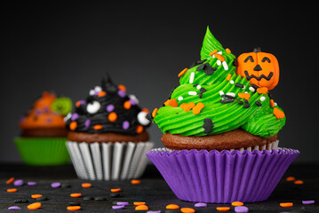 Wall Mural - Halloween cupcake. Pumpkin Jack o lantern. Dessert on Halloween party. Muffin decorated with colored frosting and Icing shaped pumpkin Jack-o-lantern. Cupcakes on wooden black background. High quality