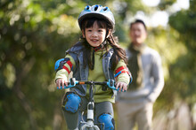 Little Asian Girl Riding Bike Outdoors In City Park