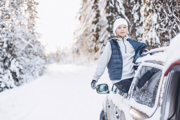 Wall Mural - Teenager boy looking out of car window traveling in winter snowy forest. Road trip adventure and local travel concept. Happy child enjoying car ride. Christmas winter holidays and New year vacation