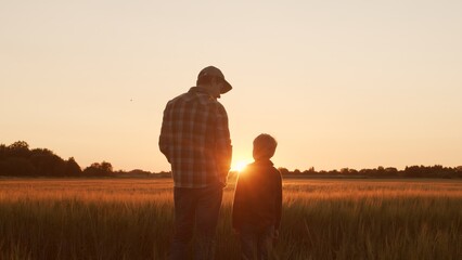 Farmer and his son in front of a sunset agricultural landscape. Man and a boy in a countryside field. Fatherhood, country life, farming and country lifestyle.