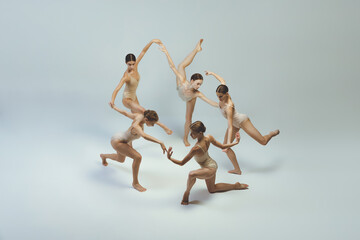Wall Mural - Group of young girls, ballet dancers performing, posing isolated over grey studio background. Circle movements