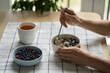 Woman eating healthy breakfast with oatmeal porridge with summer berries - cowberry, blueberry, slice of butter, herbal tea. Clean eating, dieting, weight loss concept. Shallow depth of field