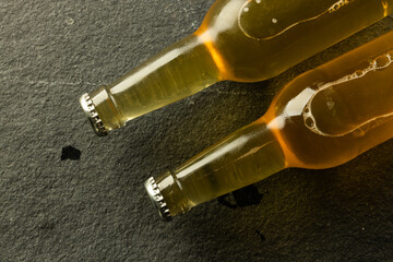 Image of two clear glass beer bottles with crown caps lying on slate, with copy space