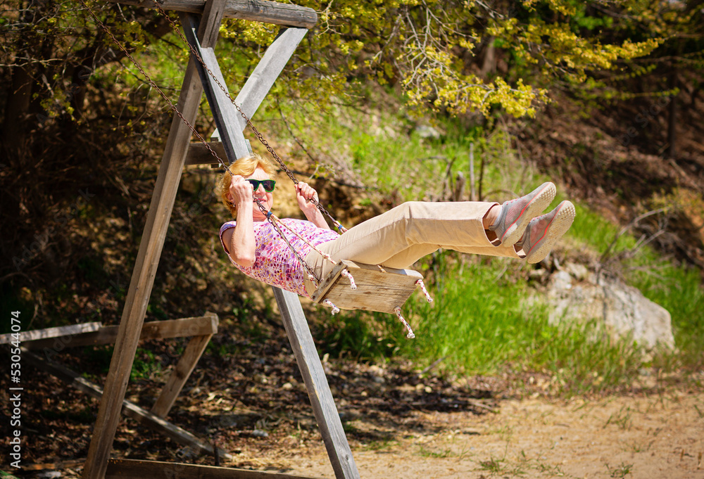 Senior woman joyfully swinging on a swing and having fan. Happy retirement concept