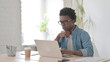 © stockbakers - Young African Man Thinking while Working on Laptop in Office