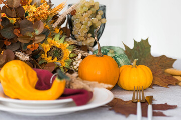 Beautiful autumn table setting. A plate with a cotton napkin and pumpkins. Table gold and a vase with autumn flowers on a linen tablecloth. The concept of festive serving for Thanksgiving.